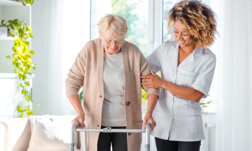 Cheerful friendly nurse helping senior woman to use walking frame