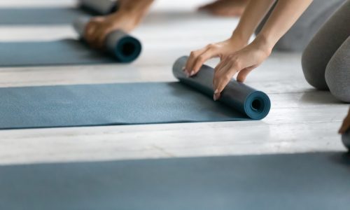 Young sporty people folding yoga mat after working out on floor in studio close up, finishing group lesson, holding rubber carpets, preparing for sport training in fitness center